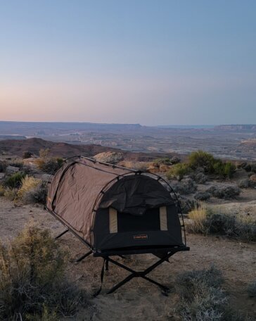 Crashpad Stealth Swag tent cot set up on a rocky overlook above a desert canyon at dusk