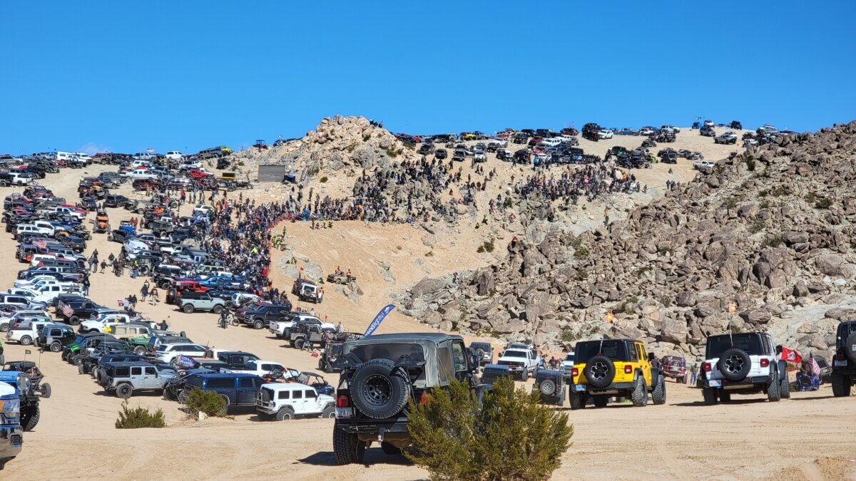Large daytime crowd and spectator vehicles parked on a rocky hillside at King of the Hammers