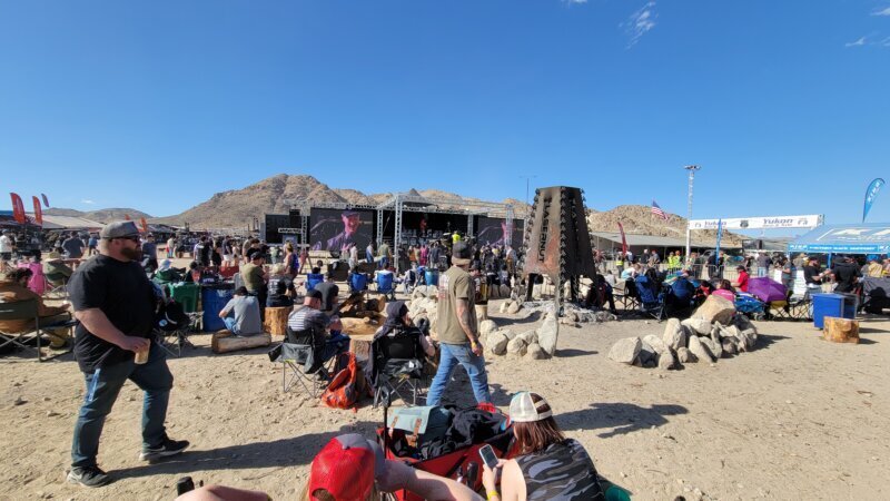 Crowd gathered at a Hammertown stage and fire pit at night during King of the Hammers