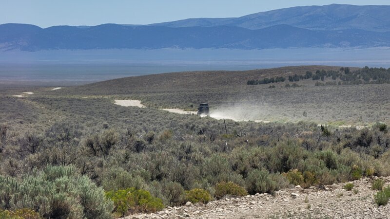 A Jeep Wrangler JKU trailing dust across a wide sagebrush valley in the White Pine Range