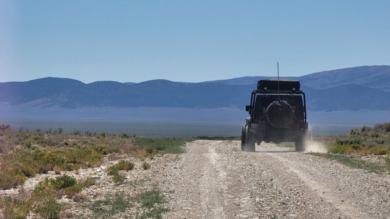 A Jeep Wrangler JKU kicking up dust on a gravel road through the White Pine Range valley