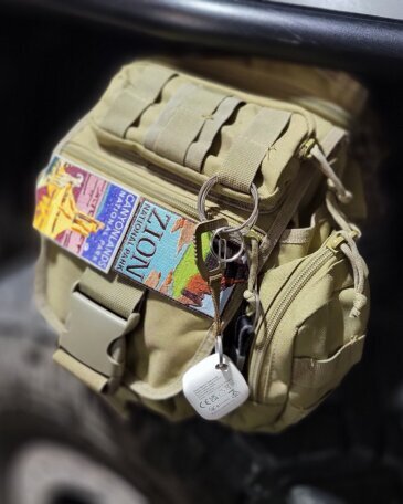 Tan EDC sling bag with Zion and Canyonlands National Park patches, keys and a smart thermo-hygrometer clipped to the zipper