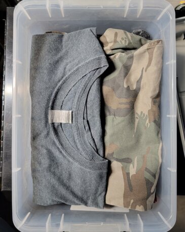 Rolled clothing packed in a clear bin, a gray hoodie and a camo jacket ready to go