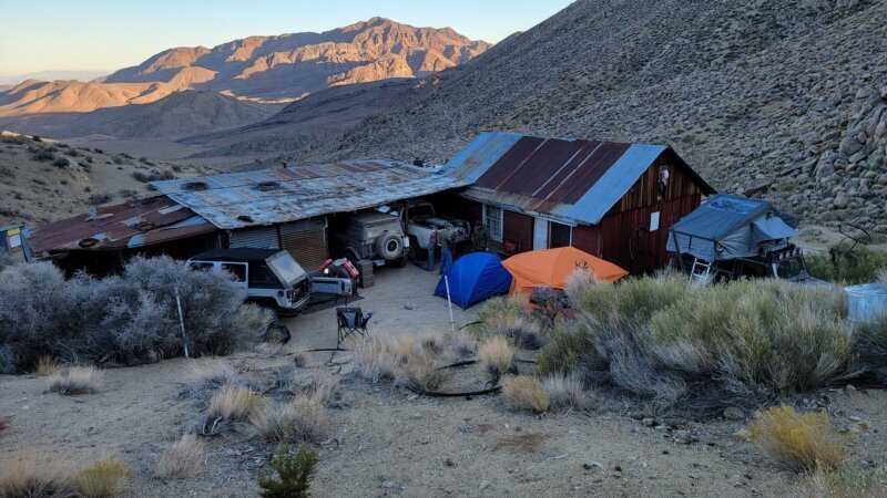 Jeeps and a rooftop tent camped in front of a well-maintained old mining cabin at the end of a rough desert trail