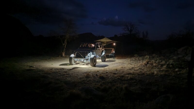 Jeep lit up by rock lights and under-vehicle lighting at a desert camp at night
